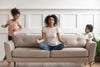 Mother Sitting on a Couch Meditating with Her Kids Playing around Her