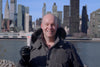 Guy Holding a Tube of Deodorant in a Winter Jacket with New York in the Background
