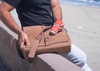 Guy Holding a Leather Laptop Bag and Natural Deodorant next to the ocean