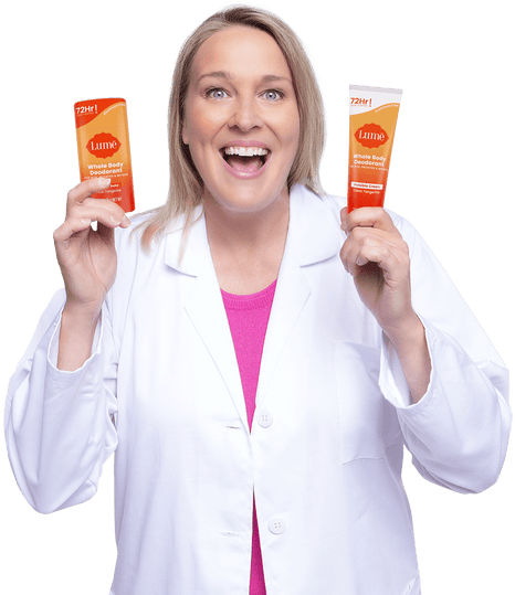Woman smiling and wearing a white doctor's coat and purple shirt while holding up a Lume deodorant stick and deodorant tube