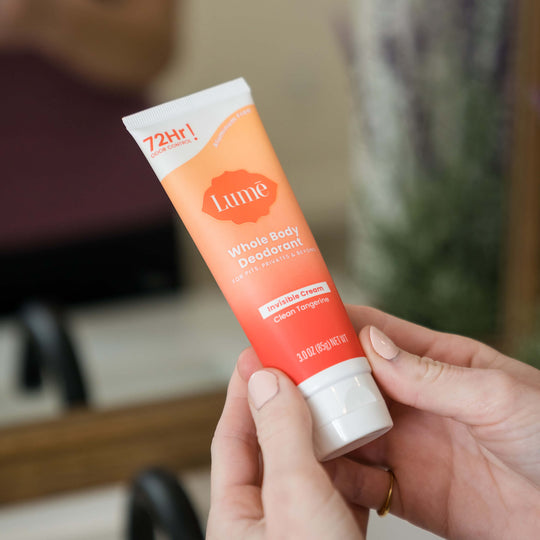 Woman hand holding a clean tangerine cream deodorant tube feet