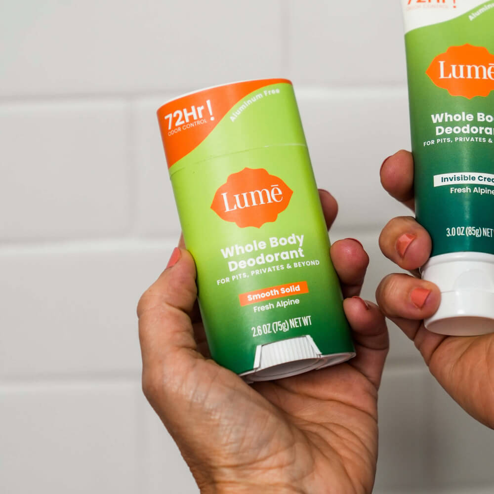 Two hands, one holding a Lume fresh alpine scented solid deodorant stick and the other a Lume invisible cream deodorant