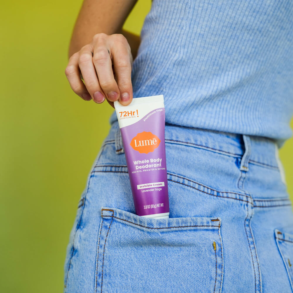 Woman in blue shirt and jeans pulling a Lume lavender sage cream deodorant tube from her back pocket