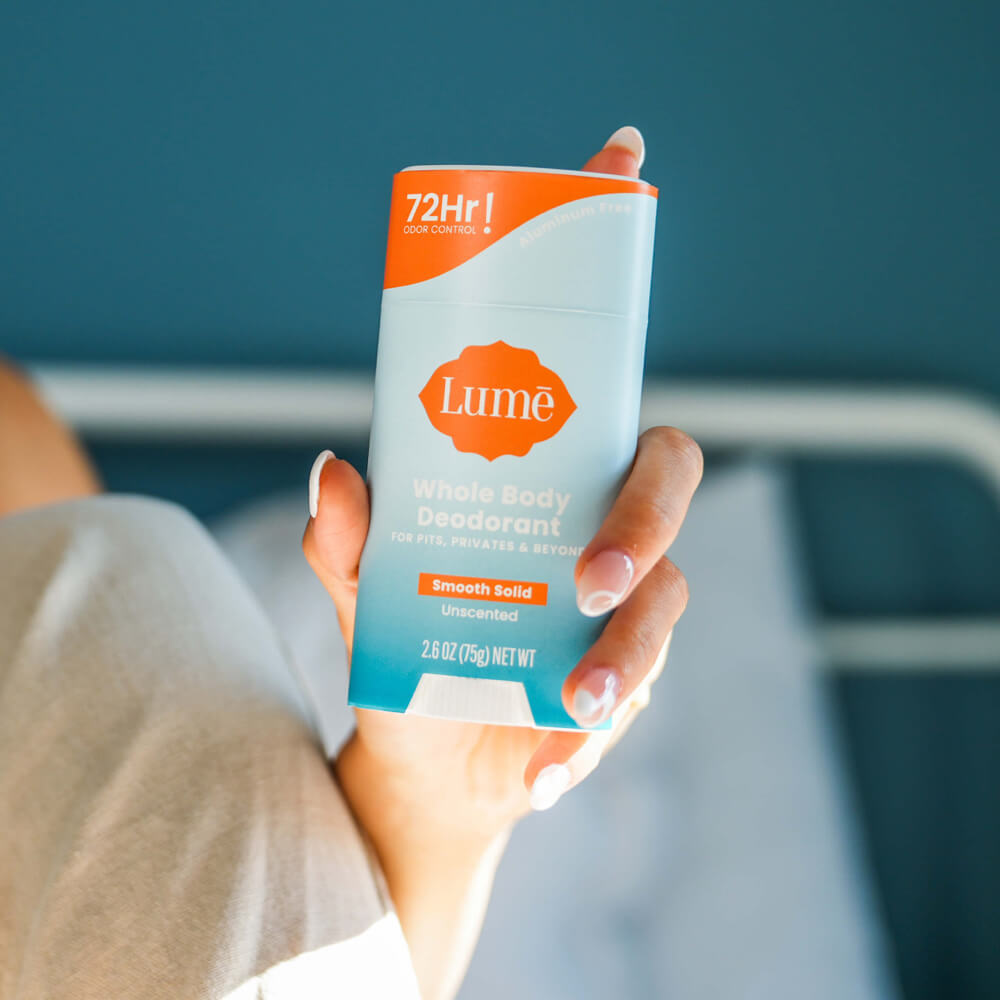 Woman holding a blue and orange bar of Lume Unscented Solid Deodorant