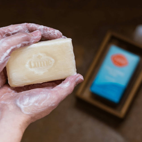 Foamy bar of Lume unscented soap in a wooden holder on a white marble counter