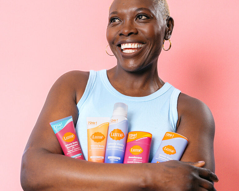 Woman holding various Lume products and smiling with arms crossed